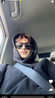 a man wearing sunglasses and a hoodie in the back seat of a car