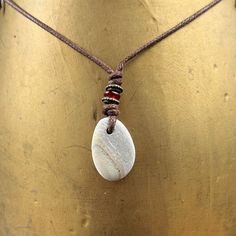 Beach pebble necklace, beige striped raw stone pendant, rock jewellery, brown cotton cord, beach found rock to wear I found this pebble on the beach in Cornwall and hung it on a brown cotton cord. The pebble is beige colour and has a faint stripes running through it I have drilled the pebble and hung it on a knotted adjustable natural coloured cotton cord  with a narrow red glass bead and two narrow bronze beads  The pebble measures approximately 27mm tall, 19mm wide and 5mm thick, the over all Brown Pendant Jewelry For Beach, Brown Pendant Jewelry For The Beach, Brown Waxed Cord Beach Necklaces, Brown Waxed Cord Necklaces For The Beach, Beach Necklaces With Brown Natural Stones, Beach Necklace With Brown Natural Stones, Beach Brown Necklace With Natural Stones, Minimalist Waxed Cord Jewelry For Beach, Handmade Cord Jewelry For The Beach