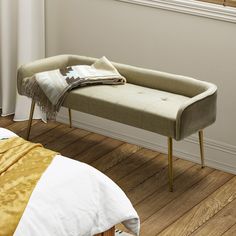 a gray bench sitting on top of a wooden floor next to a white bed in a bedroom