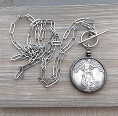 Please note - this item cannot be guaranteed to arrive for Christmas delivery. A beautiful replica antique French Victory coin cast in silver pewter is encircled in a silver plated brass coin holder with an 8mm brass ring bail. It hangs from a pewter silver paperclip style chain with a front closure oversized toggle clasp. Also available with a back closure in a lobster claw clasp. The coin with bezel measures 2 inches long X 1.5 inch wide.  Please see photo for image of reverse side of coin des Antique Silver Medallion Necklace With Locket, Heirloom Silver Necklace With Coin Pendant, Silver Medallion Necklace With Vintage Charm, Engraved Metal Medallion Coin Necklace, Antique Silver Medallion Necklace With Engraving, Antique Engraved Silver Medallion Necklace, Antique Silver Medallion Necklace With Coin Pendant, Antique Silver Engraved Medallion Necklace, Vintage Oxidized Coin Necklace