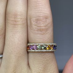 a woman's hand with a ring on it that has multicolored stones