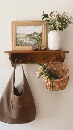 a brown purse hanging on a wall next to a basket with flowers and a painting