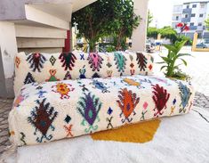 a multicolored couch sitting on top of a white rug next to a plant