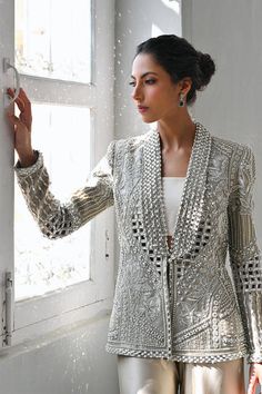 A slate coloured tissue jacket with folded lapels is rendered with intricate cutwork and thread and embroidery. Paired with ivory choli and slate-coloured charmeuse box trousers with embroidered hems; this outfit exudes sheer elegance. Model Height is 5'6 jacket length is 26" Elegant Traditional Drape Outerwear For Party, Elegant Party Outerwear With Traditional Drape, Silk Nehru Jacket With Intricate Embroidery For Reception, Elegant Formal Outerwear With Chikankari Embroidery, Elegant Silk Nehru Jacket With Chikankari Embroidery, Formal Silk Nehru Jacket With Chikankari Embroidery, Elegant Festive Outerwear With Chikankari Embroidery, Elegant Outerwear With Chikankari Embroidery For Reception, Elegant Silk Sherwani With Resham Embroidery