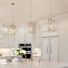 a kitchen with white cabinets and an island in front of a stove top oven that has three lights hanging from the ceiling