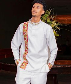 a man standing in front of a table wearing a white outfit with red and gold trim