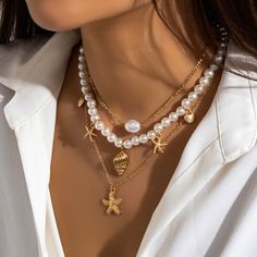 a close up of a woman wearing a necklace with pearls and gold charms on it