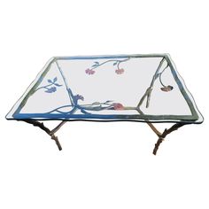 a glass coffee table with metal legs and flowers on the glass top, against a white background