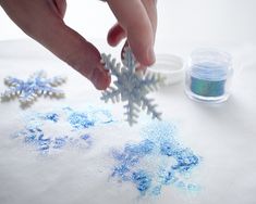 someone is making snowflakes out of powder and glue on a tablecloth with other items