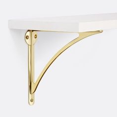 a white shelf with two gold brackets on it's sides and a light fixture in the middle