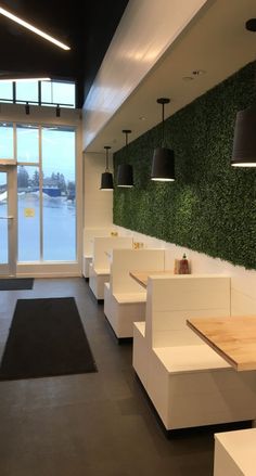 the interior of a restaurant with white booths and plants on the wall behind them,