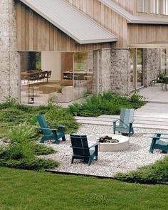 an outdoor fire pit surrounded by lawn chairs and gravel in front of a wooden building