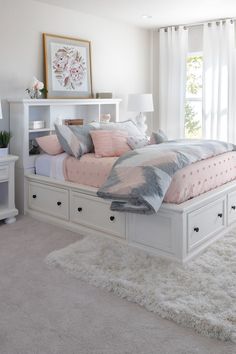 a white bed with pink and gray pillows