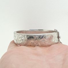 A vintage sterling silver snap bangle bracelet with engraved patterns on the front and a smooth plain back, also fitted with a safety chain. The bracelet is fully hallmarked with date letter "0" dating back to 1963. It opens and closes as it should. It measures internally from clasp too hinge approx. 5.74 cm so your wrist needs to be slimmer than this to fit when it is closed, it is approx. 16 mm wide and it weighs approx. 28 g. Condition is good true vintage. Please check out the other items in Hallmarked Vintage White Gold Bangle, Vintage Hallmarked White Gold Bangle, Victorian Silver Engraved Bangle, Victorian Style Silver Engraved Bangle, Vintage White Gold Hallmarked Bangle, Victorian Style Engraved Silver Bangle, Vintage Engraved White Gold Bracelets, Victorian Sterling Silver Engraved Wedding Bracelet, Ornate Silver Hallmarked Bangle