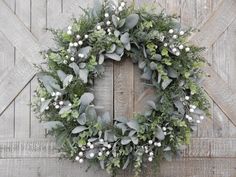 a wreath is hanging on the side of a wooden door with white flowers and greenery