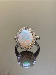 an opal and diamond ring sits on a reflective surface