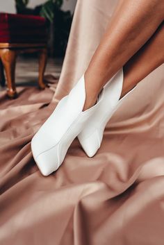 a close up of a person's legs wearing white high heeled shoes on a bed