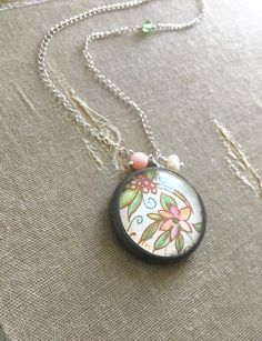 This unique handmade pendant necklace features a piece of artisanal Italian Florentine paper set behind glass in an antique gold polymer clay bezel. The sterling silver chain in adorned with Swarovski crystal, a pale pink coral bead, and a small freshwater pearl. The back of the pendant is stamped with a tiny heart.  The pendant is about one inch (~25mm) in diameter, and hangs from an 18-inch (~46cm) sterling silver chain with a spring clasp. All findings are sterling silver.  Although the necklace is sealed, it is not waterproof, so please be sure to remove it before showering, bathing, or swimming. ♥ Customers outside the US and EU, please contact me for shipping quotes ♥ More polymer clay necklace designs: http://www.etsy.com/shop/twoelements?section_id=5876615 ♥ Custom orders welcome T Whimsical Silver Glass Jewelry, Handmade Polymer Clay Round Pendant Jewelry, Handmade Whimsical Round Jewelry, Handmade Whimsical Flower Pendant Jewelry, Handmade Whimsical Jewelry, Whimsical Handmade Flower Pendant Jewelry, Whimsical Round Beads For Jewelry Making, Bohemian Polymer Clay Round Jewelry, Handmade Polymer Clay Jewelry With Flower Pendant