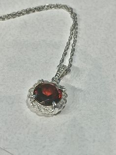 14K White Gold Diamond & Garnet scalloped Halo fancy pendant. This Halo pendant features a beautiful faceted 2.18ct round 8mm red Garnet stone, surrounded by diamonds, 0.05ctw. the chain is a 14K white gold rope chain, 1mm, 18" longThe arrangement of its facets is similar to that of a round brilliant, designed to maximize light and color. The sides are fancy scroll work with an open back. The stone is set in a 14K white gold prong setting which has an attractive halo design and holds the garnet Fancy Pendant, Scroll Work, Halo Design, Gold Rope Chains, Garnet Pendant, Garnet Necklace, Halo Pendant, Garnet Stone, Red Garnet