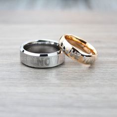 two gold and silver wedding bands with the word love written in them on a wooden surface