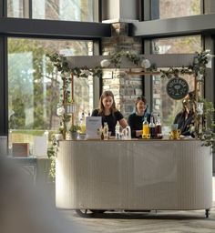 two women sitting at a bar with drinks in front of them and flowers on the counter