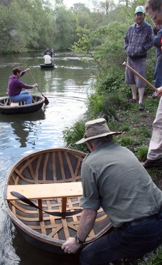 several people are in small boats on the water near some grass and trees, while one man is holding a paddle