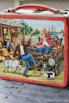 an old fashioned lunch box painted with people and dogs on it, sitting on a table