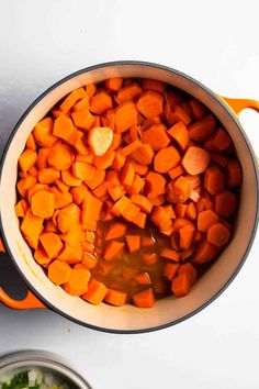 carrots and other vegetables are being cooked in an orange pot