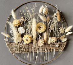 an arrangement of dried flowers in a wicker basket on a gray wall with gold rim