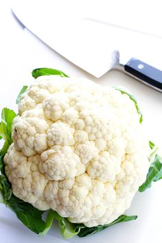 a white cauliflower sitting on top of lettuce next to a knife