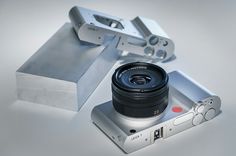 a camera lens sitting on top of a metal box next to a silver object with a white background