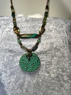 Fun, bold colorful 2" pendant with Palm Tree charm on two strands of 1mm bronze leather cord, Peacock Agate, Aventurine, India Agate and two 3/4" each Mother of Pearl. A large Genuine 1 1/2" Sea Green Turquoise Bead takes center stage bringing the colors together. Bronze toggle to close. Necklace is 22"  around neck with drop of pendant  total is 24". No lead or nickel used. Please use the Last On, First Off approach. Stones discolor with lotions, perfumes, hairspray, sweat, chlorine, even some soaps, and will break if dropped. Handmade Adjustable Turquoise Necklace With Round Pendant, Handmade Turquoise Necklace With Round Pendant, Adjustable Green Turquoise Necklace For Festival, Handmade Turquoise Necklace With Adjustable Round Pendant, Handmade Artisan Turquoise Necklace, Adjustable Double Strand Bohemian Turquoise Necklace, Turquoise Necklace With Large Pendant And Round Beads, Bohemian Green Handmade Turquoise Necklace, Green Turquoise Round Beads Necklace For Festival