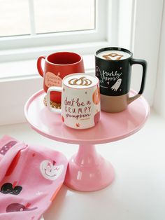 two coffee mugs sitting on top of a pink cake plate