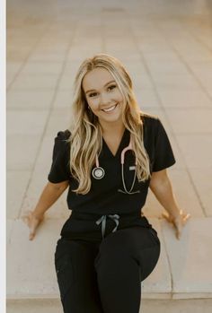 a woman in black scrubs sitting on the ground with her hands behind her back