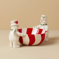 two snowmen are in a red and white striped bowl, one is holding the other's hand