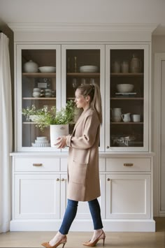 a woman walking in front of a white china cabinet