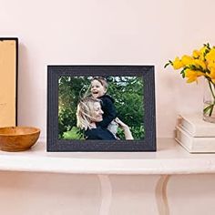 a white shelf topped with a wooden bowl filled with yellow flowers next to a black framed photo