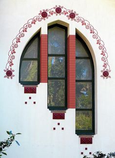 an arched window on the side of a white building with red trim and decorative windows