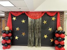 an entrance decorated with red, black and gold balloons in front of a star backdrop