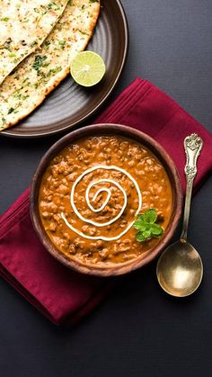 a bowl of beans and tortilla on a plate with a spoon next to it