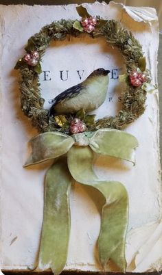 a bird sitting on top of a green ribbon next to a wreath with flowers and leaves