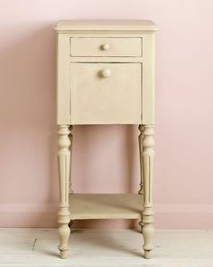 a small white table with drawers against a pink wall