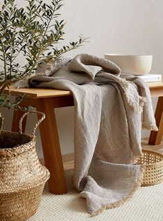 a table with a bowl, basket and blanket on it next to a potted plant