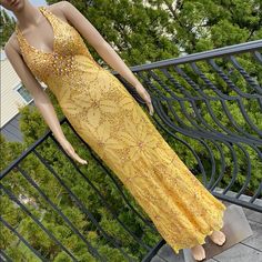 a mannequin dressed in a yellow dress on a balcony overlooking some trees and bushes