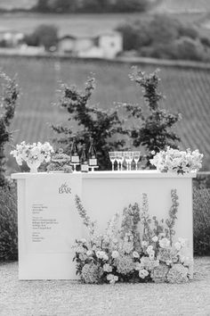 an outdoor bar with flowers and wine glasses on the table in front of some bushes