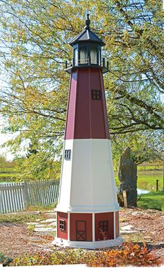 a red and white light house sitting in the middle of a park next to a tree