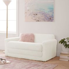 a living room with a white couch and pink throw pillow on the floor next to a painting