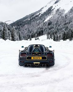 a black sports car parked on top of snow covered ground in front of a mountain