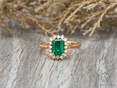 an emerald and diamond ring sitting on top of a wooden table next to some branches