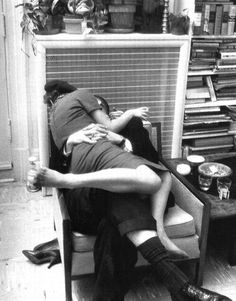 a man and woman laying on top of each other in a room full of clutter